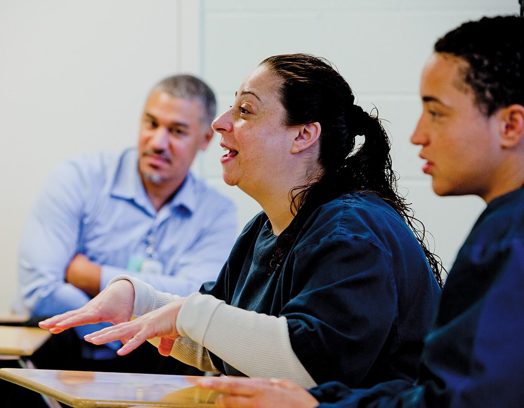 Bridge Program participant Julie Robat (center) confers with her classmates in the Rhode Island women’s unit, including Merissa Piccoli. Monteiro, as usual, is a quiet but respected figure in the background—a living symbol to his incarcerated peers that real change is possible.