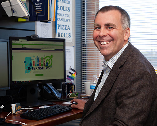 Mike Slocum of Indiana INTERNnet smiling at desk in an office high rise. A tablet, charter, and gay pride flag can be seen in his work environment.