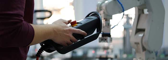 Stock photo of a human controlling a robot with a handheld remote.