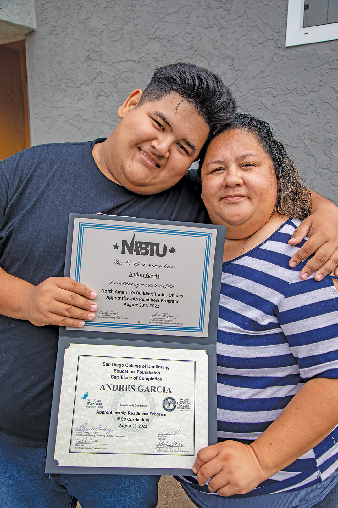 Two people in a side hug showing a certificate made out to Andres Garcia.