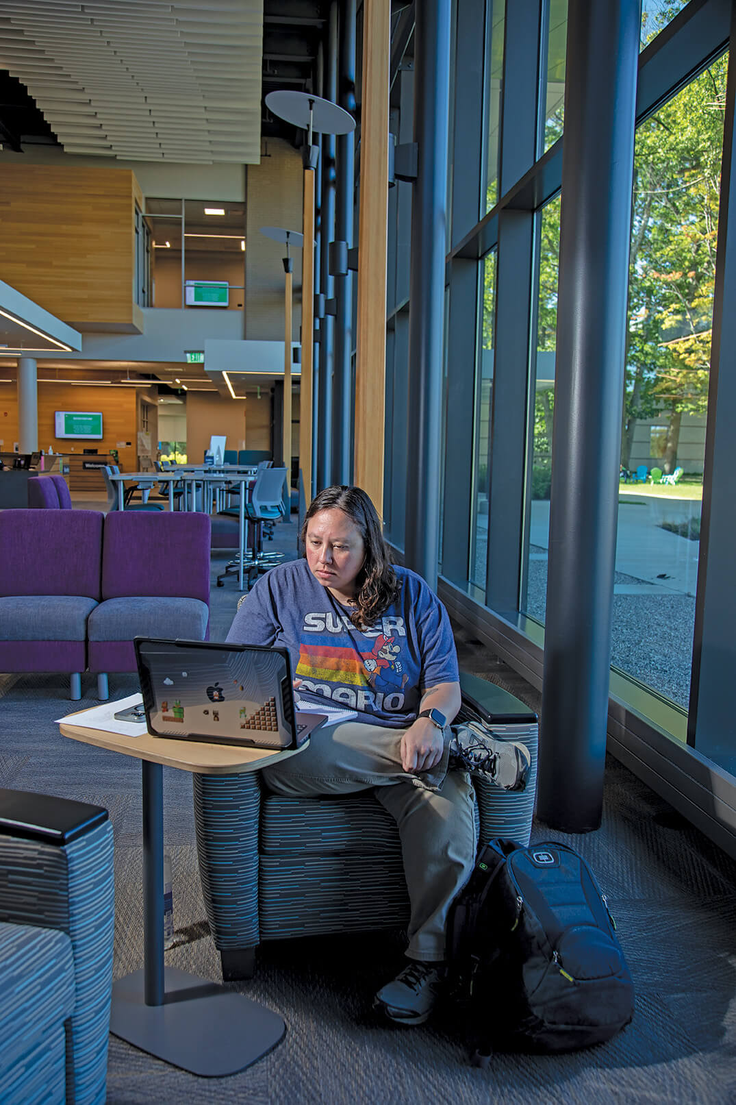 Woman from before is now inside the building seated with her laptop.